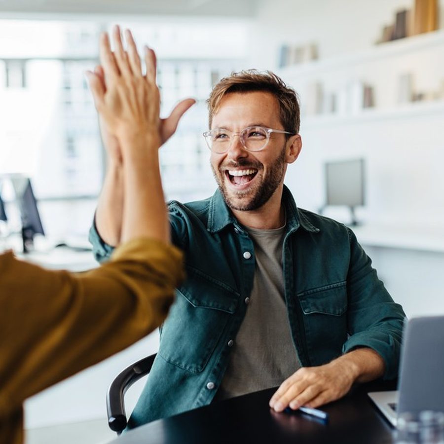 Two colleagues laughing and high-fiving in the office
